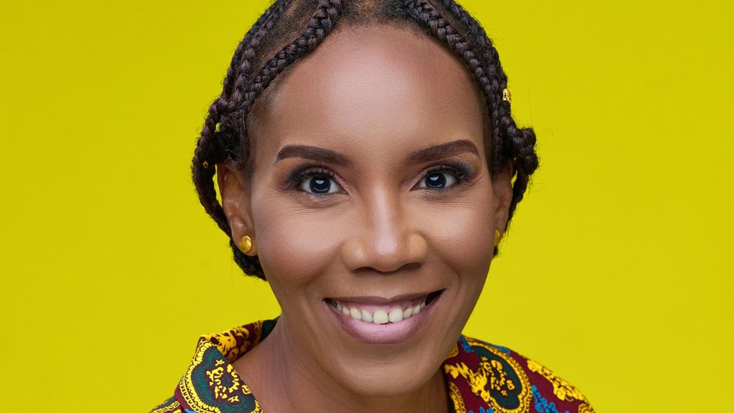 Headshot of Blessing Musariri, a Black woman in her 30s or early 40s, wearing braids and a patterned shirt, smiling against a lime green backdrop. 