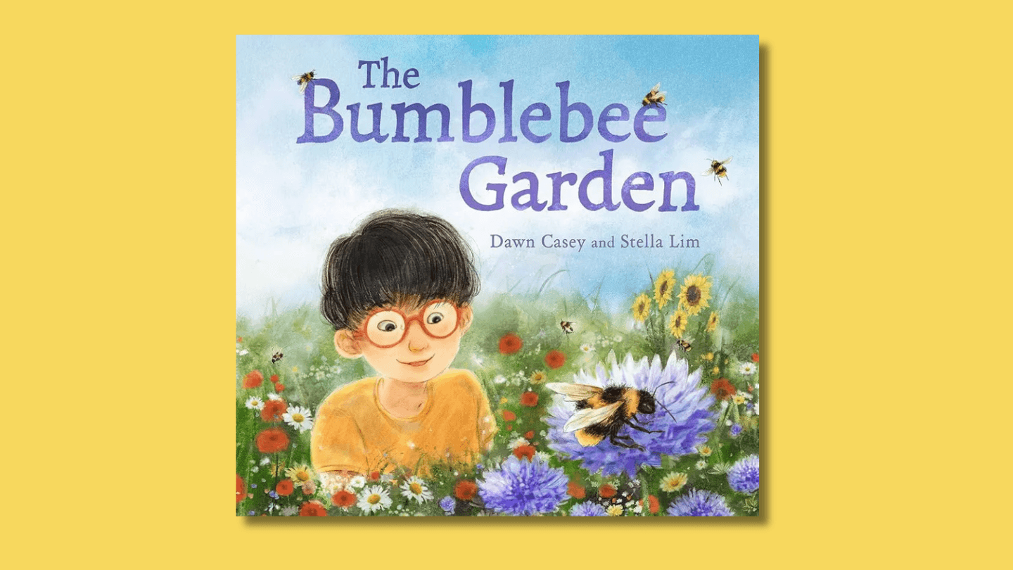 The cover of The Bumblebee Garden shows a young boy with East Asian heritage, wearing red glasses, in a garden bursting with flowers, gazing spellbound at a large bumblebee on a purple flower.