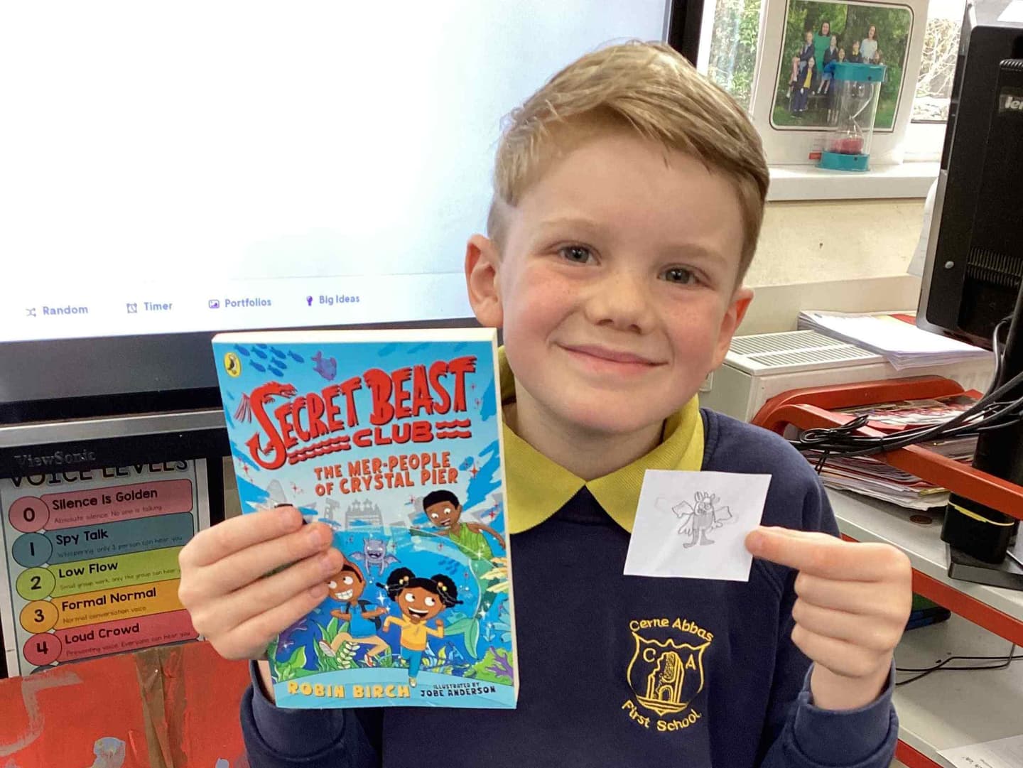 A broadly smiling young white boy holds up a copy of Secret Beast Club, a book about 2 young Black mystery-solvers.