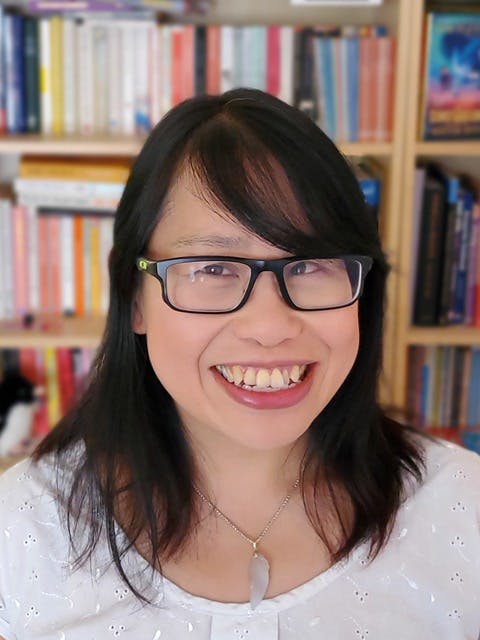 A head-and-shoulders photograph of Wendy, a forty-five-year-old British Chinese woman, is standing in front of a bookshelf. She is smiling and wearing a white top and glasses.